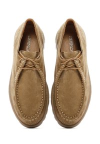 Zapatos estilo mocasín de ante marrón con punta redondeada, costuras blancas en contraste y suelas de goma marrón con textura antideslizante.