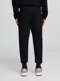 Pantaloni da ginnastica neri con vita elasticizzata, gamba affusolata e polsini a costine. Abbinati a scarpe da ginnastica sportive grigie e bianche.