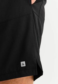 Schwarze athletische Shorts mit glatter Textur, ausgestattet mit perforierten Seitenpaneelen und einem kleinen silbernen Logo an der unteren Seite.