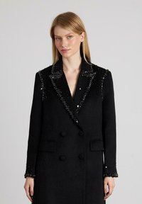 Abrigo de lana negro con diseño de doble botonadura, adornado con lentejuelas en el collar y los puños, con bolsillos de solapa y un corte ajustado.