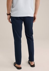 Marineblauwe slim-fit broek van lichtgewicht stof, met een zachte textuur en details langs de tailleband, gecombineerd met zwarte instapsandalen.