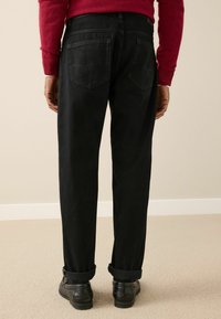 Black denim trousers with a straight-leg fit, featuring rolled cuffs, two rear pockets, and subtle stitching details. Waterproof leather shoes.