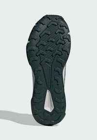 Terrængangsko sål med en struktureret sort gummioverflade. Har aggressive studs for traction og et strømlinet design.