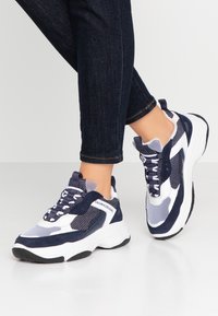 Calvin Klein Jeans sneakers med en kombination av marinblå mocka och vit mesh, med en kraftig vit sula och kontrasterande svart gummisula.