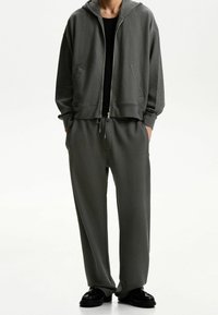 Grå texturerad hoodiekappa med matchande byxor, med framfickor, dragkedja och avslappnad passform. Svart fotbeklädnad fulländar looken.