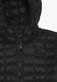 Czarna pikowana kurtka z kapturem, z przednim zamkiem błyskawicznym i haftowanym logo "The North Face" na piersi.