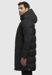 Sort puffers jakke med hætte, quiltet design, sidelommer og længere snit. Glat overflade, med en minimalistisk stil og uden synlige mønstre.