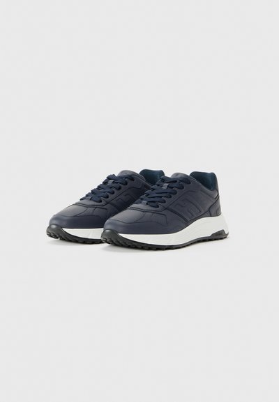 Un paio di sneaker in pelle blu navy con suole spesse bianche e suole esterne testurizzate nere, dotate di logo in rilievo sui lati e lacci blu.