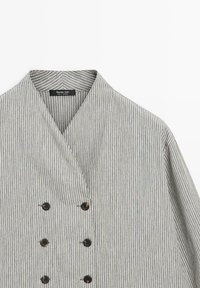 Graue und weiß gestreifte Jacke mit Schalkragen, doppelt geknöpft und aus leichtem Stoff. Schwarze Knöpfe sorgen für Kontrast.