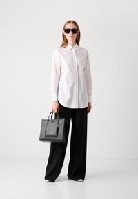 Camicia bianca con bottoni, pantaloni neri a gamba larga, occhiali da sole neri oversize e una borsa nera strutturata con tasca frontale. Texture lisce.