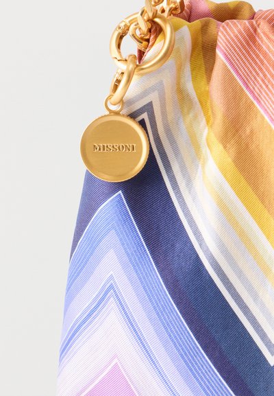 Χρυσό μπρελόκ Missoni προσαρτημένο σε υφασμάτινο ύφασμα με πολύχρωμο σχέδιο ζιγκ ζαγκ σε αποχρώσεις μπλε, κίτρινου, ροζ και λευκού.