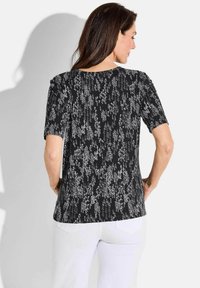 Haut noir à manches courtes avec un motif abstrait texturé argenté. Doté d'un col rond et d'une coupe décontractée. Fabriqué en tissu léger.