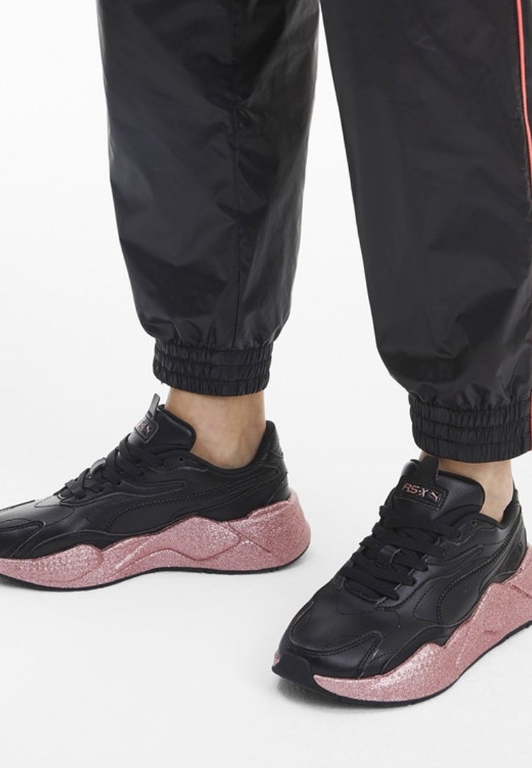 Zapatilla negra con parte superior de cuero texturizado y gruesa media suela de purpurina rosa, con un diseño curvado y cordones negros.