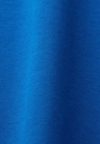 Gros plan sur une texture de tissu bleu lisse avec un motif fin en tricot et des plis doux créant des variations de lumière et d'ombre.