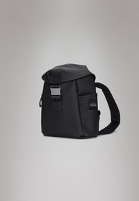 Mochila preta com acabamento mate, topo arredondado e uma alça texturizada. Apresenta uma fivela metálica e um bolso lateral para armazenamento.