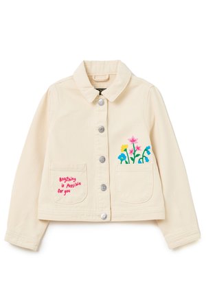 Roomwitte jas met zilverkleurige knopen, twee voorzakken, bloemrijke borduring op één zak en rode tekst "Alles is mogelijk voor jou" op de andere.