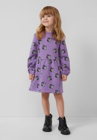 Paarse lange mouw jurk met een ronde hals en een zwart-wit wolfprint. Het heeft een geplooide taille en geribbelde manchetten, gecombineerd met zwarte laarzen.