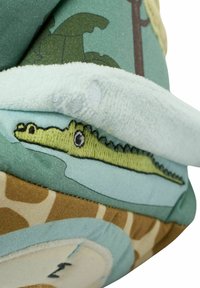 Kék anyagon zöld krokodil hímzéssel díszített plüss állat, puha türkiz akcentusokkal, bézs dzsungelmintával és plüss textúrával.
