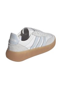 Zapatilla blanca con acentos en azul claro, materiales de gamuza y cuero, suela de goma gruesa y diseño clásico de tres rayas.