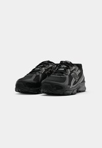 Des chaussures de sport noires avec une tige en maille texturée, une semelle rembourrée et un design à lacets. Présente un branding discret dans une teinte contrastante.