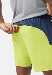 Neon gula sportshorts med midjeband i marinblått, med en sidoficka med dragkedja och en slät yta.