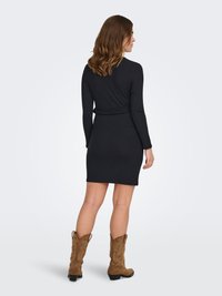 Robe noire en maille côtelée à manches longues, silhouette ajustée, longueur mi-cuisse, associée à des bottes de cowgirl couleur taupe.