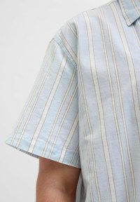 Camisa de manga corta en tejido azul claro con finas rayas verticales blancas y marrones. Presenta un cuello clásico y un ajuste relajado.