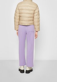 Beige pufferjacka med quiltat mönster, kombinerad med lavendelfärgade sweatpants med vita sidostängsel och bakficka. Kraftiga svarta stövlar.