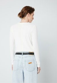 Vit långärmad T-shirt med rund halsringning, kombinerad med ljusblå denimjeans med ett svart bälte och en "DENIM"-logotyp på bakfickan.