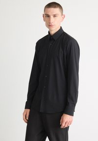 Svart langermet skjorte med krage, laget av glatt stoff, med slim fit og subtil glans, sammen med svarte bukser.