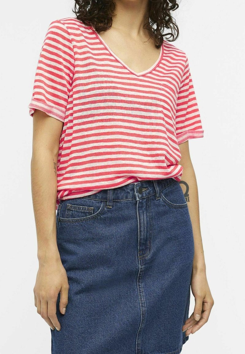 Personne portant une chemise à manches courtes rayée rouge et blanche rentrée dans une jupe en jean bleue taille haute avec des poches.