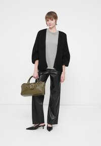 Egy nő fekete kötött kardigánt, szürke pólót, fekete bőrnadrágot és hegyes orrú fekete magassarkú cipőt visel, miközben egy olíva zöld kézitáskát tart, amelyen csillag alakú charm található.