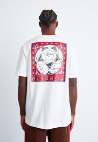 Hvid bomulds-T-shirt med en grafisk print på bagsiden, der viser en fodbold og farverige kantdetaljer. Korte ærmer; afslappet pasform.
