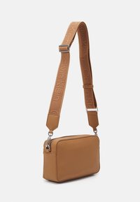 Beigefarbene, rechteckige Crossbody-Tasche aus strukturiertem veganem Leder, mit silbernen Beschlägen und einem verstellbaren Riemen, der mit "Calvin Klein" geprägt ist.