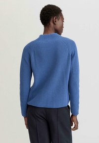 Un pull en tricot bleu avec une texture côtelée, présentant un col haut et des manches longues, vu de dos sur un fond neutre.