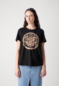 T-shirt nera a maniche corte, con un ricamo circolare di farfalla in rosa, oro e bianco su sfondo nero.