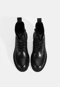 Zwarte leren enkellaarsjes met ronde neus, vetersluiting aan de voorkant en een rits aan de zijkant. Kenmerken een gladde textuur en een rubberen zool voor grip.