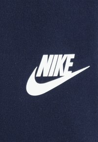 Ναυτικό μπλε ύφασμα με εμφανές λευκό λογότυπο Nike με σχεδιασμό σφύρας. Το υλικό φαίνεται λείο και πλεκτό.