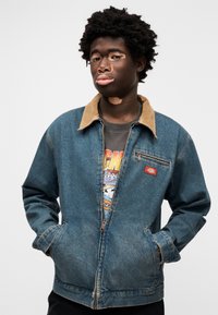 Τζιν μπουφάν με καφέ γιακά από κορδόνι, φερμουάρ μπροστά, δύο πλευρικές τσέπες και τσέπη στο αριστερό στήθος, με κόκκινο λογότυπο.