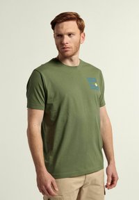 Camiseta de algodón verde oliva con cuello redondo, mangas cortas y un estampado gráfico en azul que dice "GAME SET MATCH" en el pecho.
