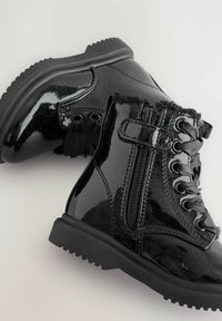 Schwarze Lackleder-Ankle-Boots mit strukturiertem Obermaterial, vorderem Schnürverschluss, seitlichem Reißverschluss und einer robusten Sohle mit tiefen Profilierungen.
