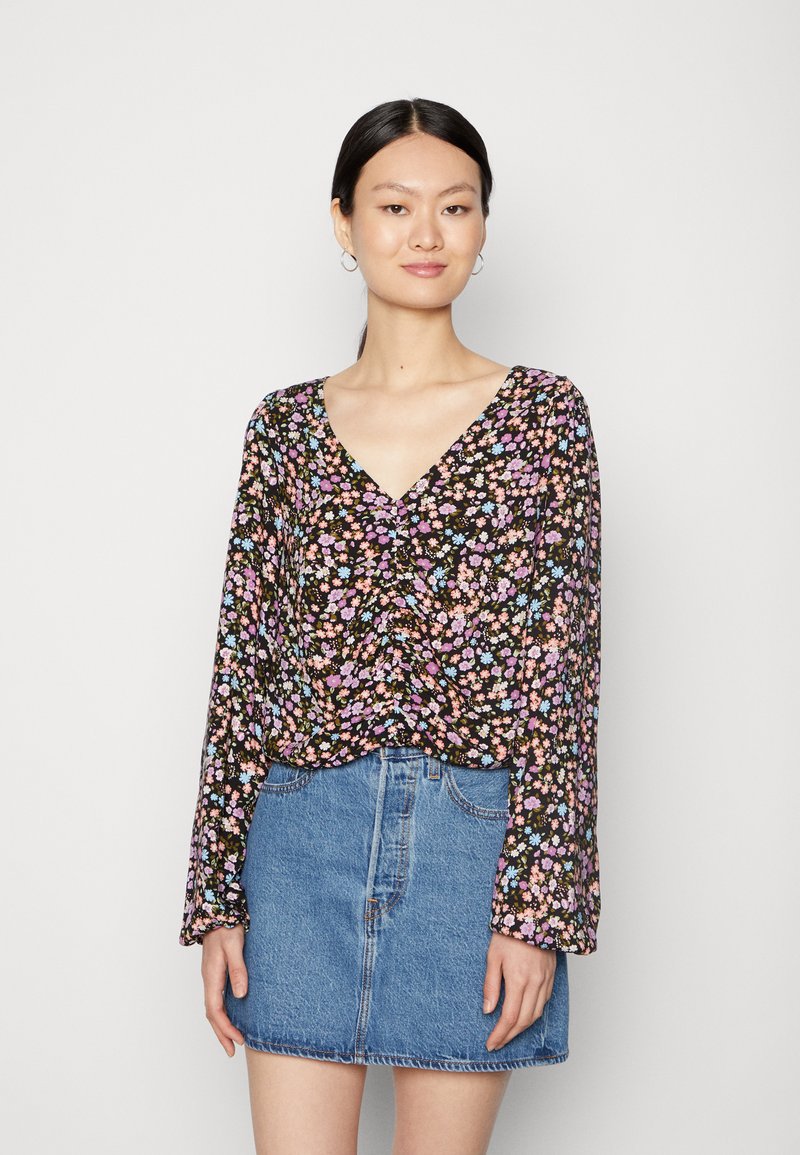 Blusa floral com decote em V, mangas longas, fundo preto, padrão de flores multicoloridas, combinada com uma saia mini de denim clara.