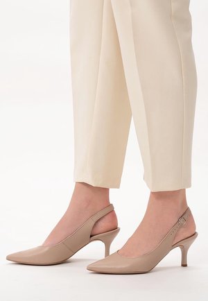 Beige spidse slingbackhæle båret med lyse cremefarvede skræddersyede bukser, der viser ankel og underben.