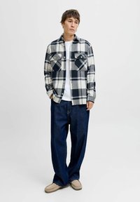 Camisa de franela de cuadros en azul marino y blanco, con dos bolsillos en el pecho, cierre de botones en la parte delantera, y combinada con unos jeans oscuros de corte holgado.