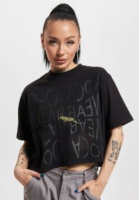Černé zkrácené tričko s texturovaným designem a nápisem "ROC A WEAR" v různých opacitách, krátké rukávy a kulatý výstřih.