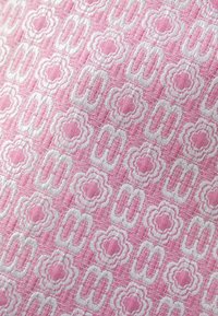 Tissu rose texturé avec un motif répétitif de fleurs blanches dessinées en contour et de formes à double boucle en rangées alternées.