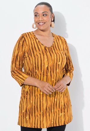 Túnica de manga larga en tela amarillo-naranja con rayas verticales marrones y puntos redondos. Escote en V y diseño de corte relajado.