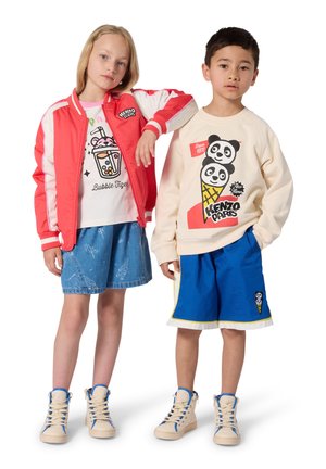 Zwei Kinder stehen nebeneinander und tragen farbenfrohe Freizeitoutfits mit Grafikprints und High-Top-Sneakers vor einem weißen Hintergrund.