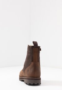 Stivale alla caviglia in suede marrone con tacco in pelle marrone, linguetta e suola in gomma testurizzata. Foderato con materiale morbido vicino alla parte superiore.