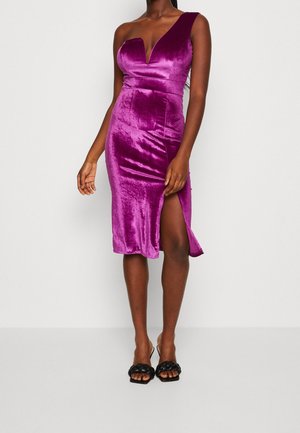 Woman wearing a shiny purple one-shoulder midi dress with a thigh slit and black braided heeled sandals.